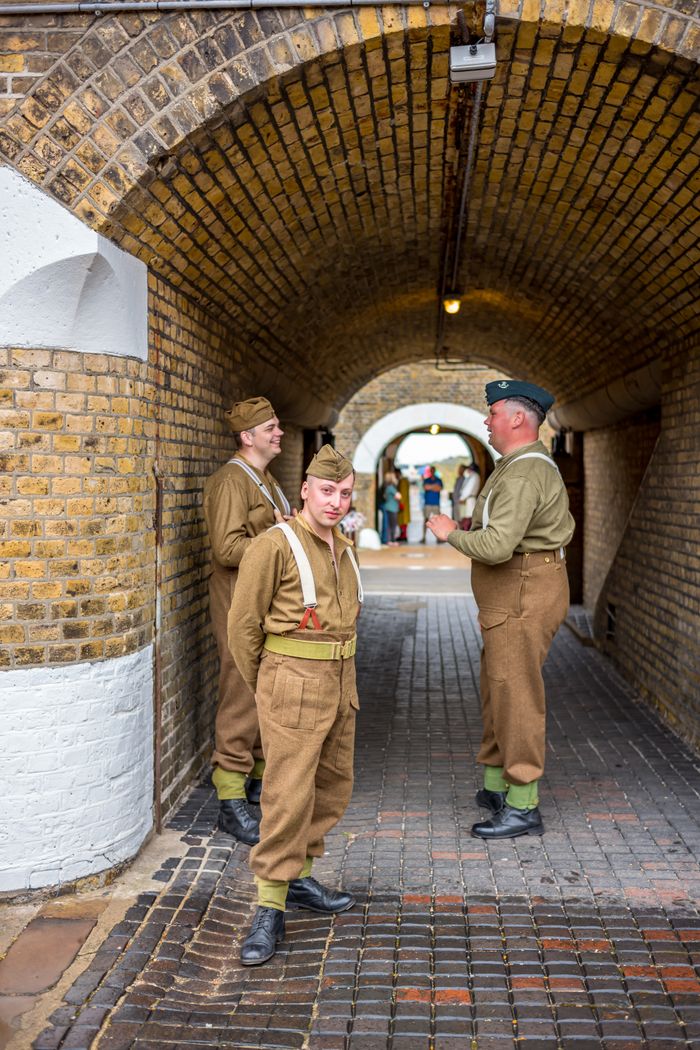 Men in vintage military uniforms reenact a historical scene in a brick tunnel.