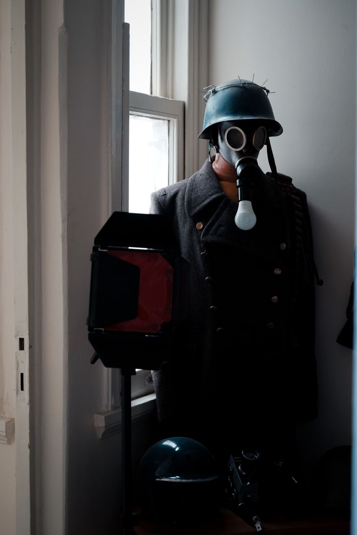 A vintage military gas mask and coat displayed in a dimly lit museum corner, alongside a tactical helmet.