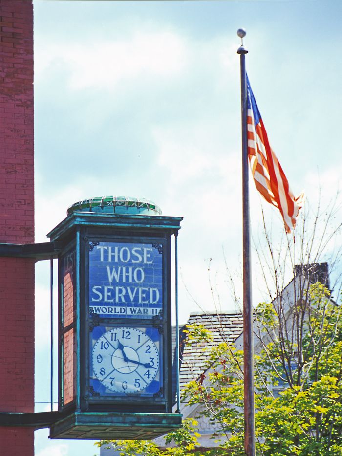 A memorial clock honoring WWII veterans with an American flag in the background.